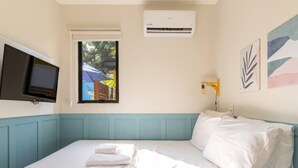 A bedroom with a bed, a television, an air conditioner, and a window with a view of a building and trees. - Parking|1000Mbps|A/C|Smart TV|Pool (Florianópolis)