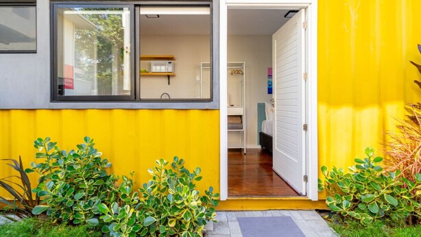 A yellow building with a sliding glass door leading to a room with a bed and a small table. - Parking|1000Mbps|A/C|Smart TV|Pool (Florianópolis)