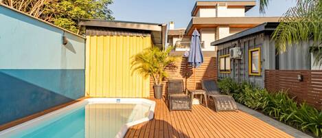 A swimming pool with a wooden deck, lounge chairs, and a covered seating area.