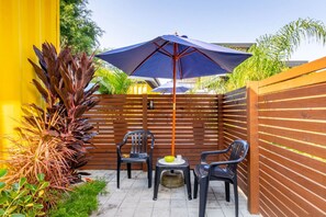 Un espace patio agrémenté d’une clôture en bois, de deux chaises, d’une petite table ronde et d’un parasol bleu.