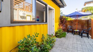 En gul bygning med et stort vindue, et træhegn og en terrasse med stole og et bord.