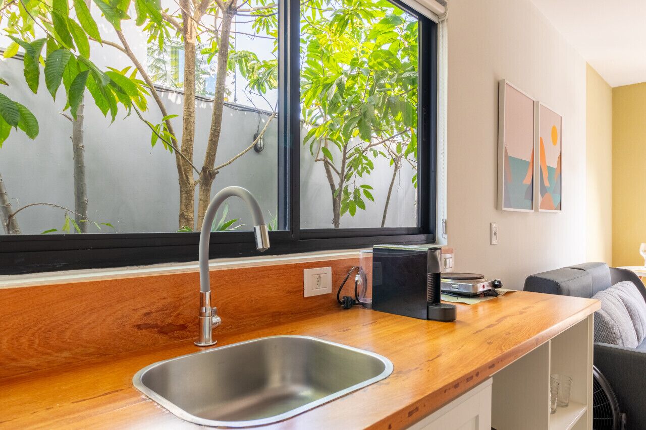 Uma cozinha moderna com pia de aço inoxidável, bancada de madeira e janela com vista para árvores.