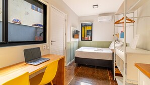 A compact room with a bed, a desk with a laptop, a chair, a wardrobe, and a window with a view of a building. - *Self Check-In*A/C*Full Kitchen*10min->Beach* (Florianópolis)