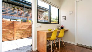 A small, bright room with a wooden desk and two yellow chairs, a window, and a view of a fenced outdoor area. - *Self Check-In*A/C*Full Kitchen*10min->Beach* (Florianópolis)