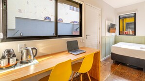 Una habitación con un escritorio de madera, una computadora portátil, una cama y una ventana con vista a edificios.