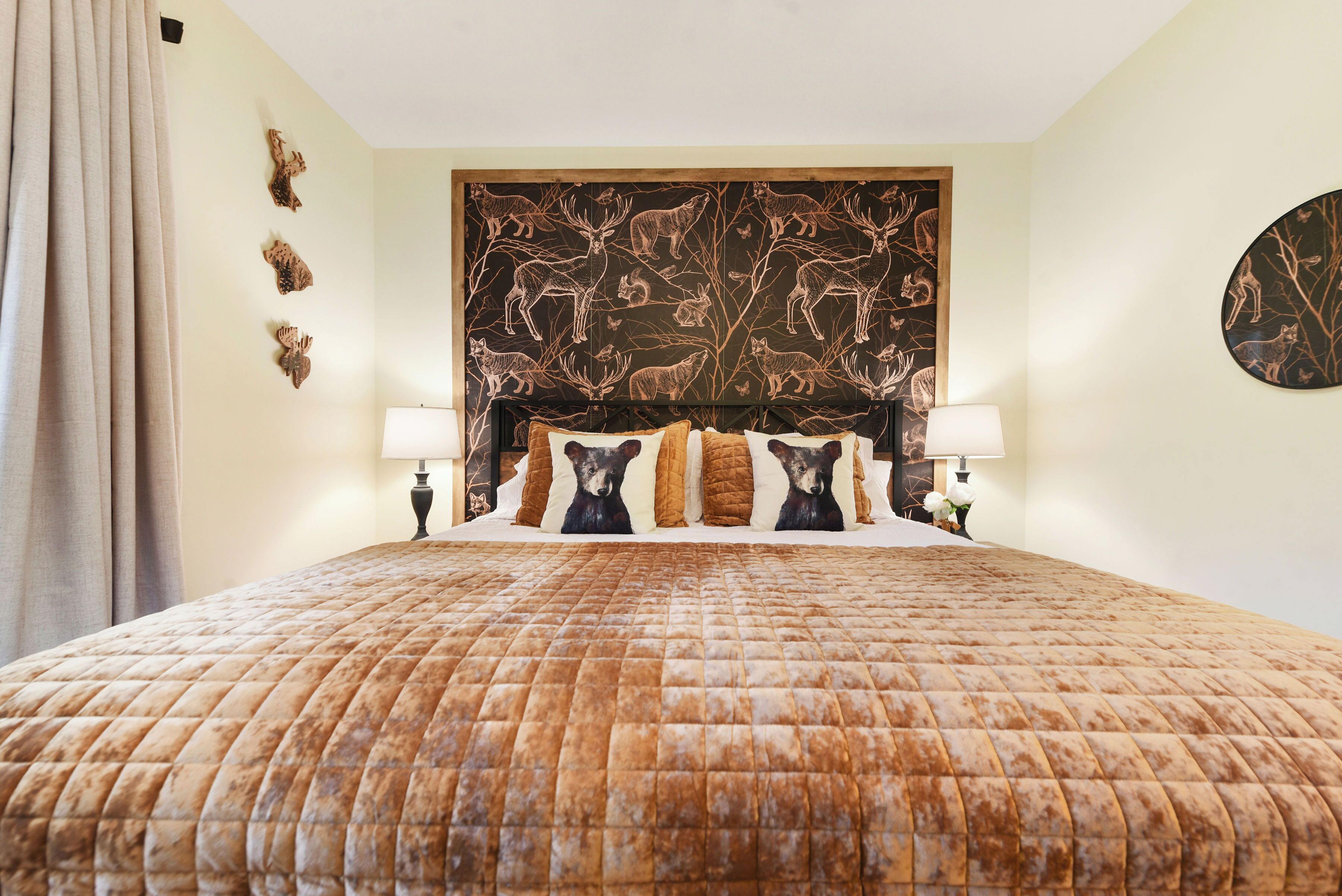 A bedroom with a large bed, a headboard with animal prints, two bedside lamps, and a wall clock.