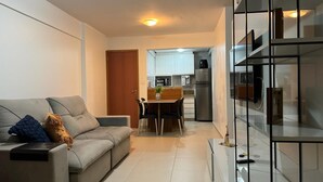 Een moderne woonkamer met een grijze bank, een eettafel met stoelen, en een keuken op de achtergrond.