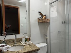 Een badkamer met een granieten aanrechtblad, een wit toilet, een douchecabine van glas en een spiegel met houten lijst.