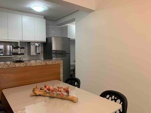 Een moderne keuken met witte kasten, roestvrijstalen apparatuur en een eethoek met een houten tafel en stoelen.