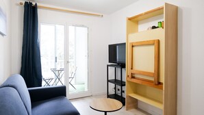 A modern living room with a sofa, a small round table, a television, and a wooden shelf unit.