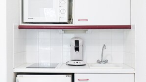 A compact kitchen with a microwave, coffee maker, sink, and a small refrigerator.