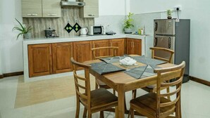 Una cocina compacta con armarios de madera, una mesa de comedor con cuatro sillas, un microondas, un hervidor y un refrigerador.