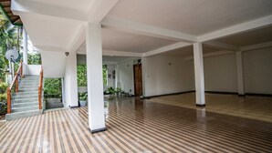 Un espacio interior amplio con suelo de madera, pilares blancos y una escalera que lleva a un área exterior con plantas.
