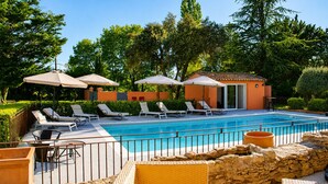 Ein Poolbereich mit Liegestühlen, Sonnenschirmen und einem kleinen Gebäude.