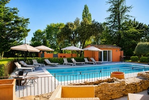 A pool area with lounge chairs, umbrellas, and a small building.