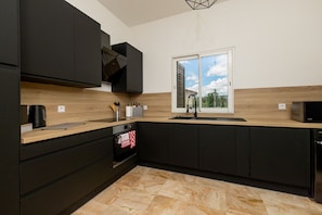 A modern kitchen with black cabinets, a wooden countertop, a built-in oven, and a window with a view of greenery.