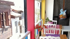Un balcón con una mesa de madera, sillas blancas y un camino de mesa morado.
