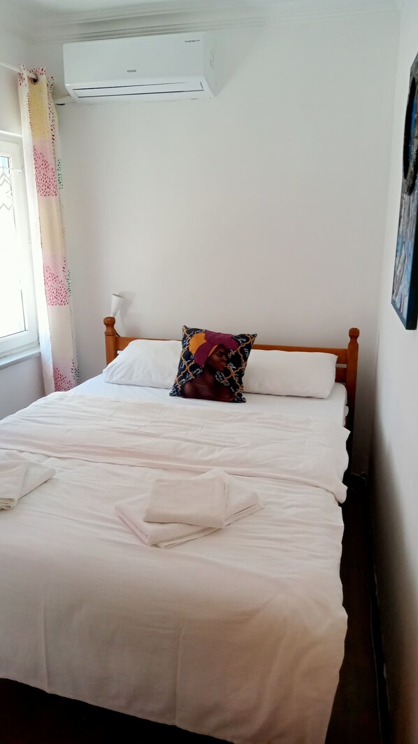 A neatly made bed with white linens, a colorful pillow, and a white towel on the floor. - Martı Butik Otel Bozcaada (Bozcaada)