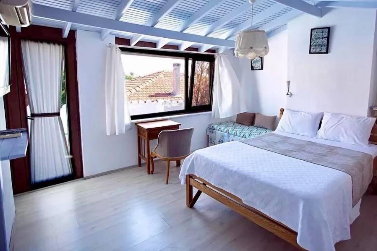 A bedroom with a bed, a desk, a chair, a window with curtains, and a ceiling fan.