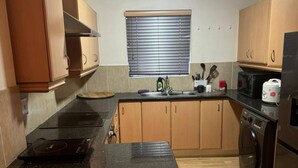 Una cucina con mobili in legno, un piano di lavoro nero, un lavello, una finestra con persiane e un forno a microonde.