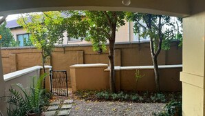Un'area patio esterna con pavimento piastrellato, un angolo relax con una sedia e un tavolino, e una pianta in vaso.