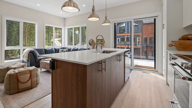 Een moderne keuken met een centraal eiland, grote ramen en uitzicht op buiten.
