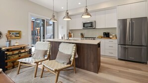 Een moderne keuken met een centraal eiland, roestvrijstalen apparatuur, hanglampen en uitzicht op het buiten.