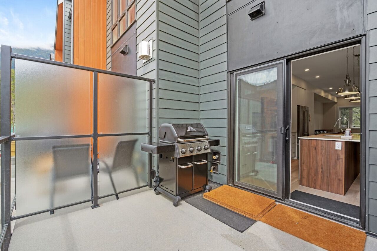 Une cuisine extérieure moderne dotée d’un barbecue, d’une porte-fenêtre coulissante et d’un banc en bois.