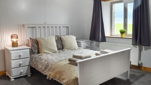 A bedroom with a white bed, a bedside table with a lamp, a window with curtains, and a radiator. - New House Farm - UKC6912 (Cowan Bridge, near Kirkby Lonsdale)