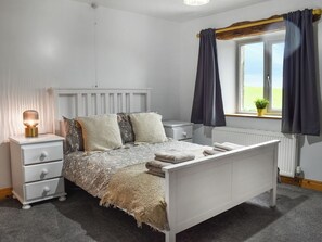A bedroom with a white bed, a bedside table with a lamp, a window with curtains, and a radiator. - New House Farm - UKC6912 (Cowan Bridge, near Kirkby Lonsdale)