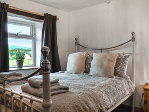 A bedroom with a bed, curtains, a window with a view, and a bedside table.