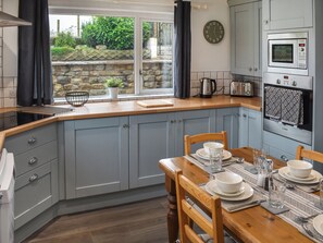 A kitchen with grey cabinets, a wooden countertop, a dining table set with plates and glasses, and a clock on the wall. - New House Farm - UKC6912 (Cowan Bridge, near Kirkby Lonsdale)