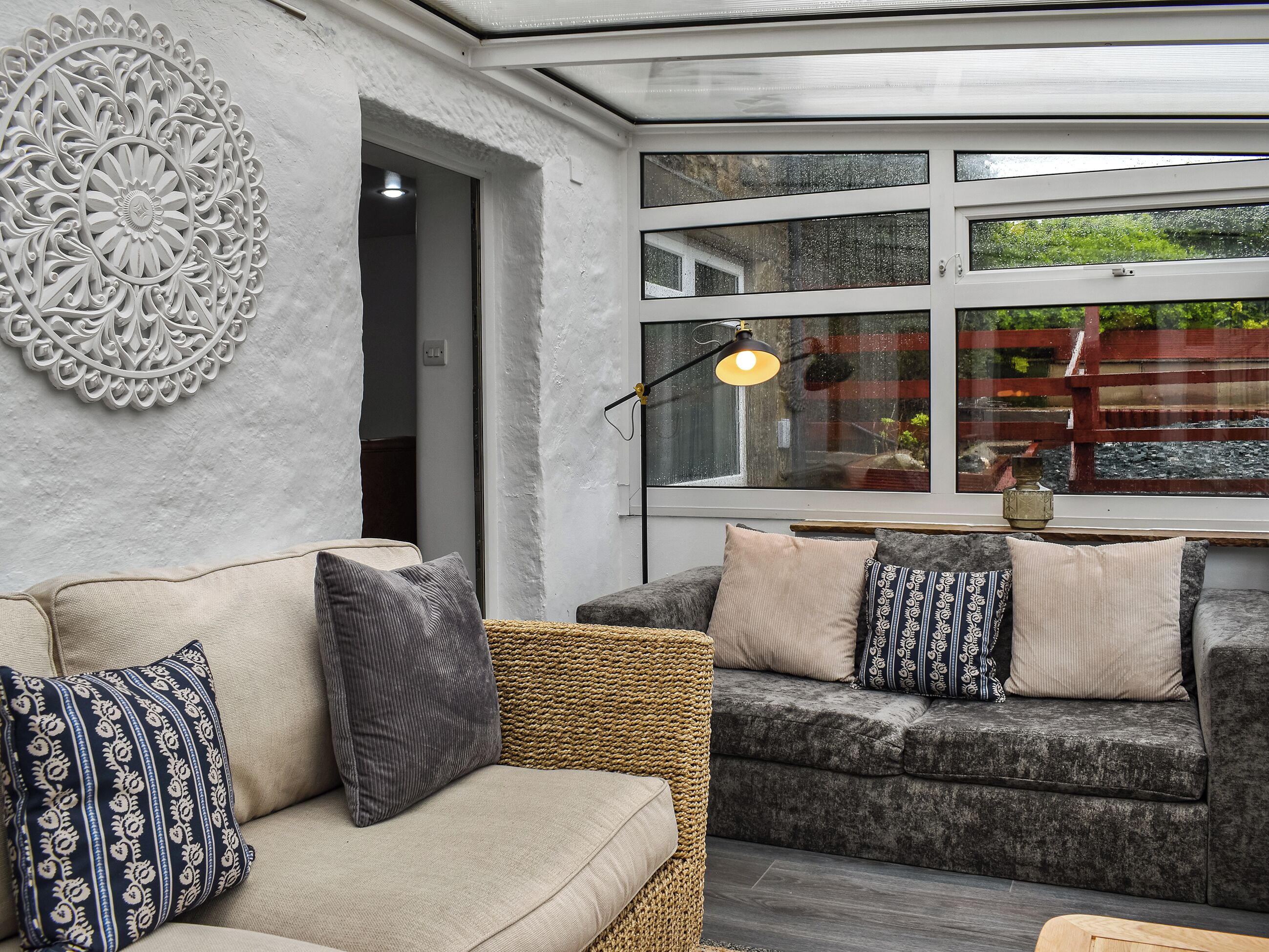 A modern living room with two sofas, a decorative wall piece, and a large window with a view of greenery.