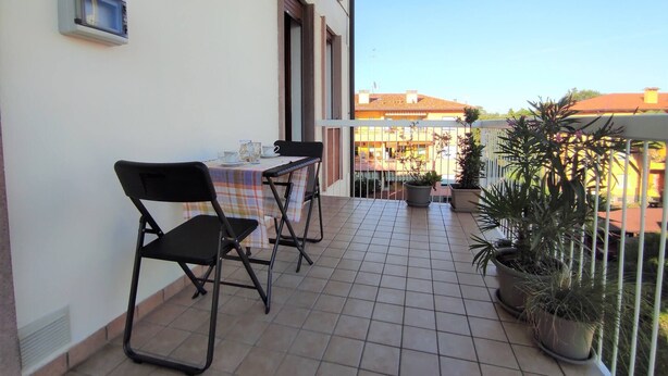 Un balcon avec une table et des chaises, des plantes en pot et une vue sur des bâtiments au loin.