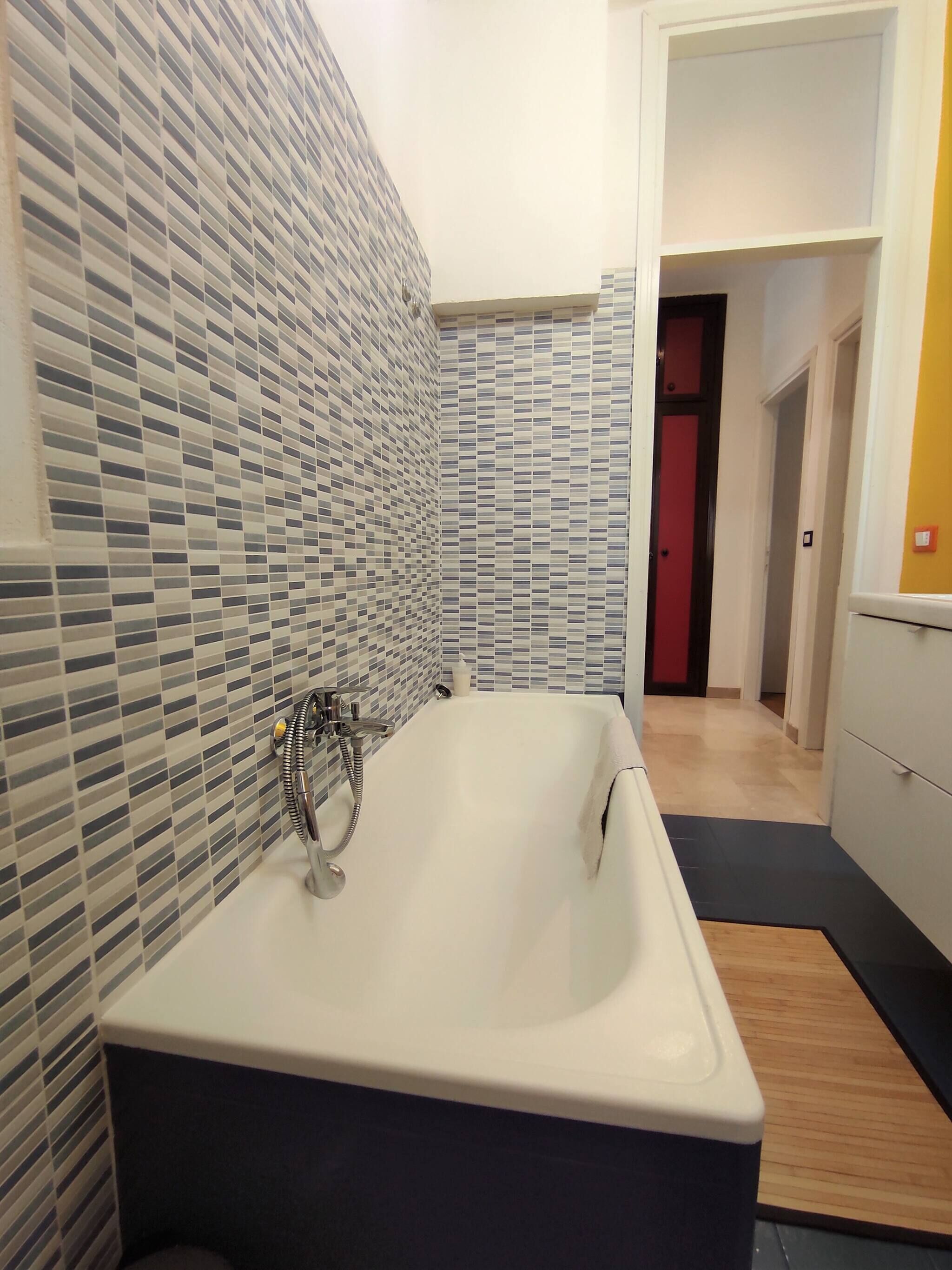 A modern bathroom with a freestanding bathtub, tiled walls, and a wooden floor.