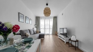 A modern living room with a sofa, TV, and dining area with a table set for two.