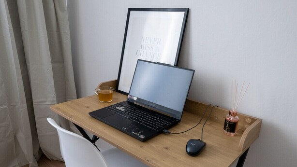 A wooden desk with a laptop, a framed quote, a glass of tea, and a reed diffuser.