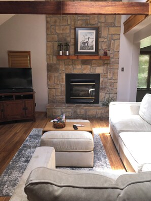 A living room with a stone fireplace, a television, and a white sofa.