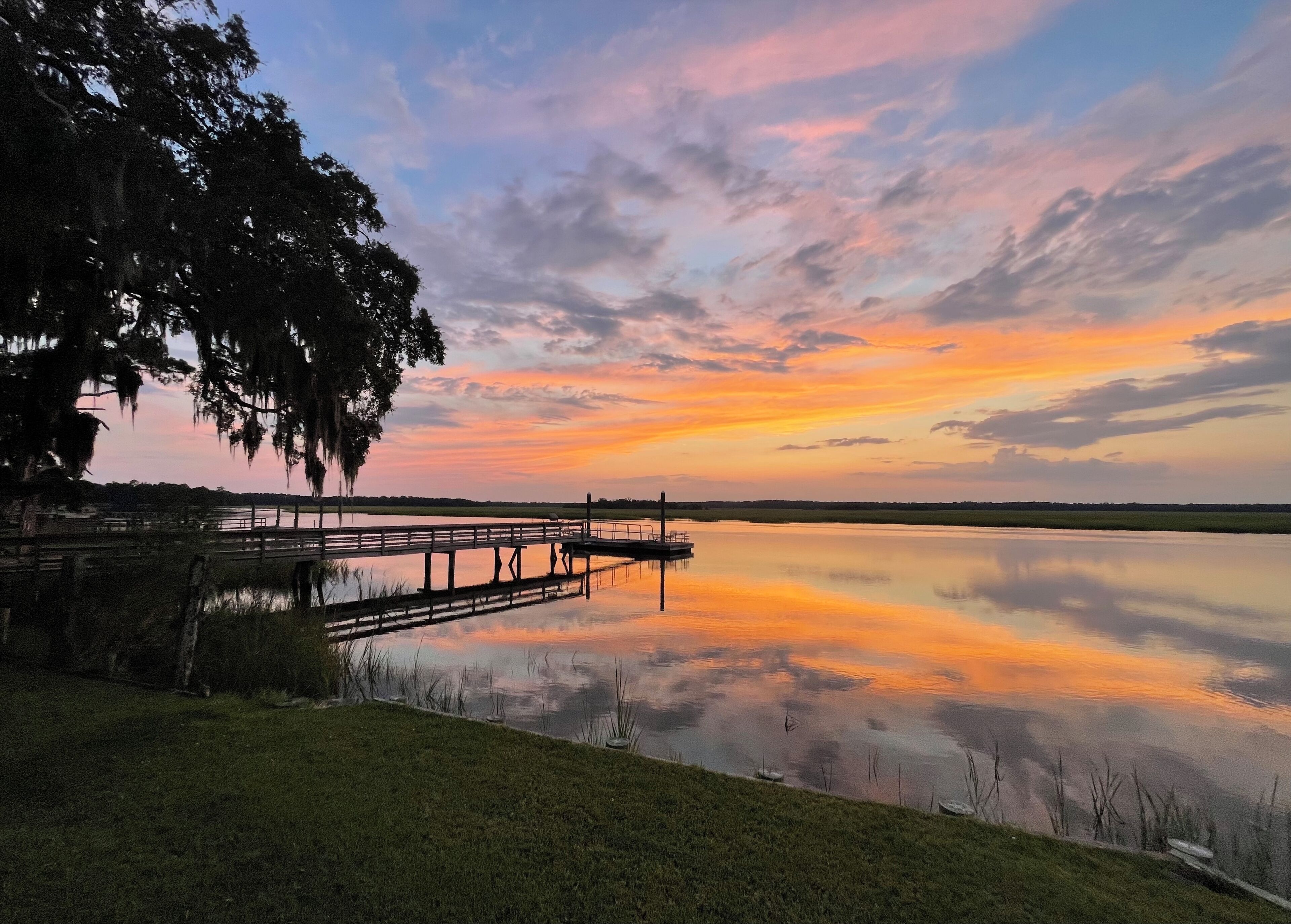 A calm lake at sunset with a wooden dock extending into the water.