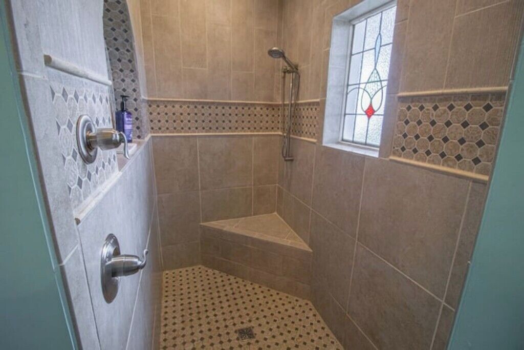 A corner shower with a small window, tiled walls, and a door with a handle.