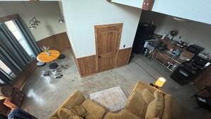 Un vaste espace de vie comprenant un grand canapé, une table à manger avec des tabourets, un coin cuisine et une porte en bois.