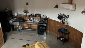 Une cuisine compacte équipée d’une cuisinière, d’un four à micro-ondes et d’un évier intégrés. Un petit coin repas est aménagé avec un canapé et une table basse.