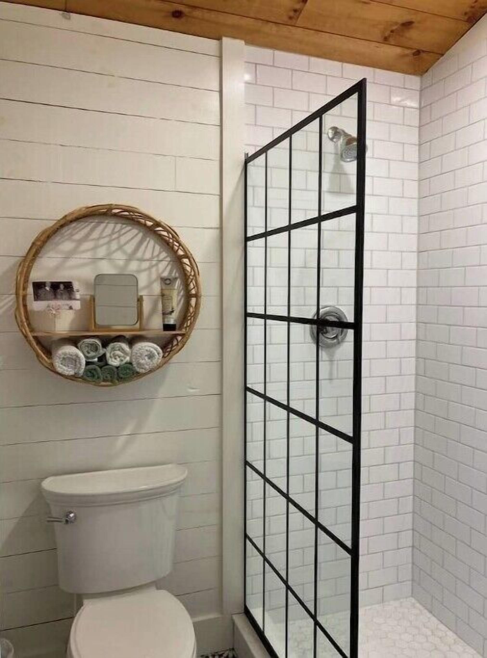 A bathroom with a white toilet, a glass-enclosed shower with black framing, and a wall-mounted mirror with a wicker frame.