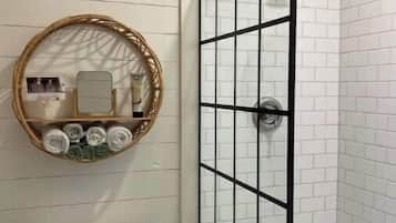 A bathroom with a white toilet, a glass-enclosed shower with black framing, and a wall-mounted mirror with a wicker frame.