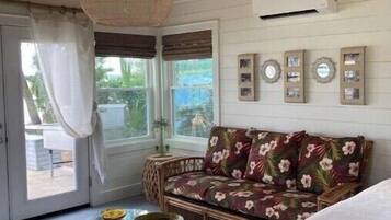A cozy room with a wooden ceiling, a floral sofa, a glass coffee table, and a bed with a white blanket.