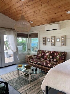 A cozy room with a wooden ceiling, a floral sofa, a glass coffee table, and a bed with a white blanket. - Paradise on the water. (Midway)