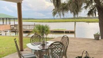 A covered patio with a table and chairs, overlooking a body of water and a grassy landscape.