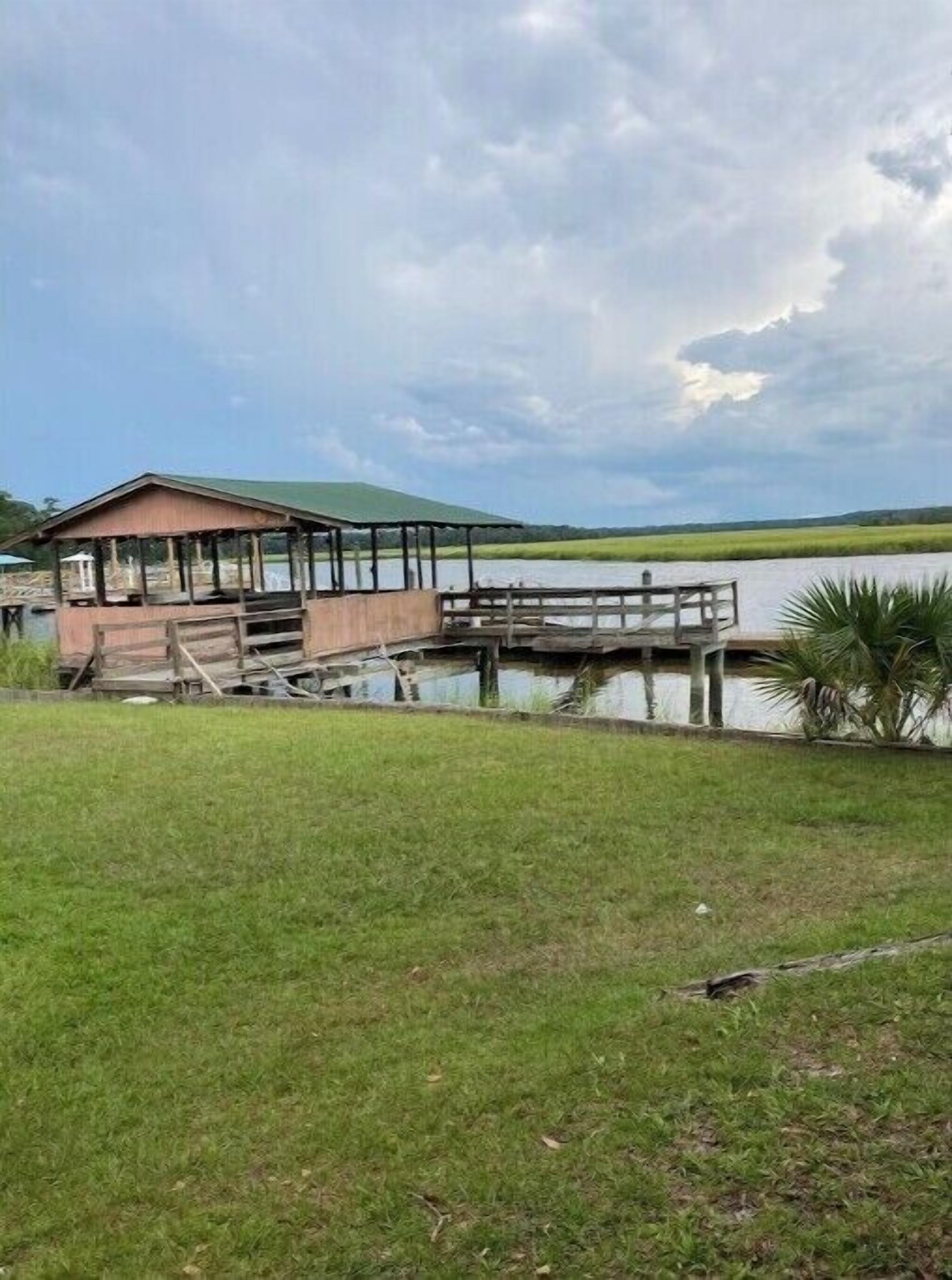 A wooden dock extending into a lake with a covered pavilion on the left.