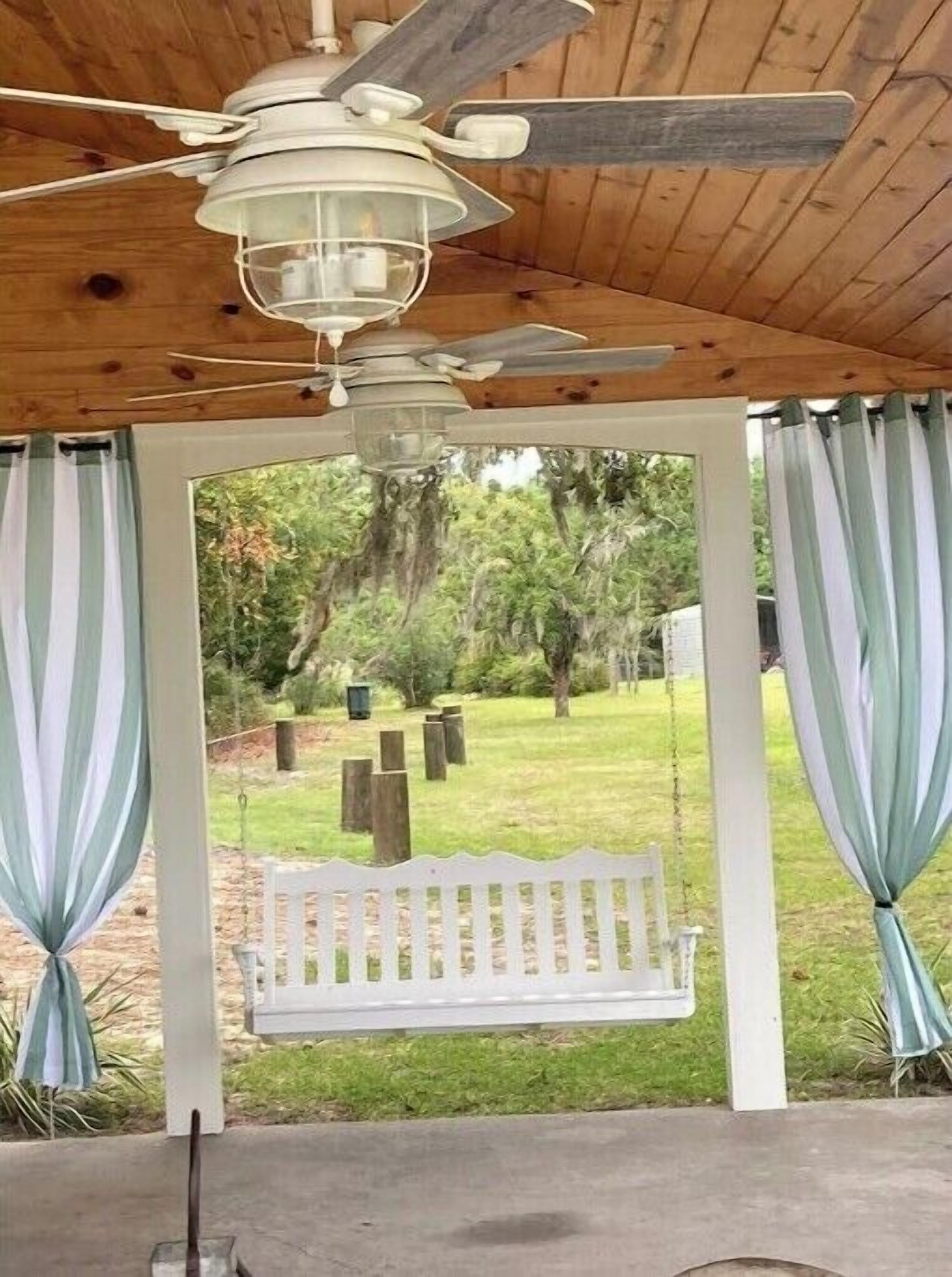 A covered outdoor seating area with a swing, wooden ceiling, and a view of a grassy yard.