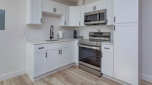 A modern kitchen with white cabinets, a stainless steel microwave, a built-in oven, and a coffee maker. - 2Br Harry Potter Themed Home 7mins from Universal (Orlando)